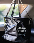 A black dry kine bucket with text 'ALOHA XCHNG' on it, hanging in a vehicle's interior.
